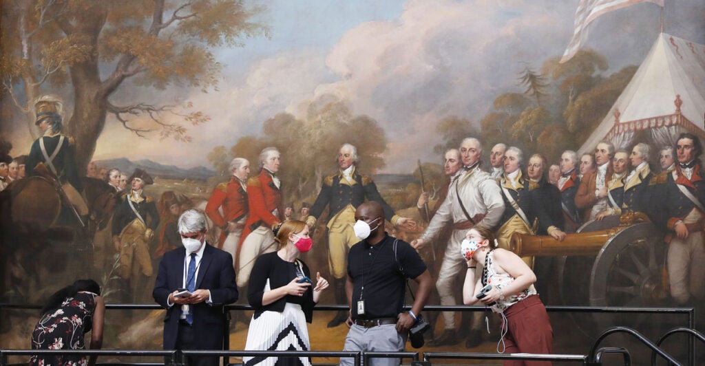 Members of the media, wearing COVID masks, stand before John Turnbull's famous painting "Surrender of General Burgoyne" in the U.S. Capitol.