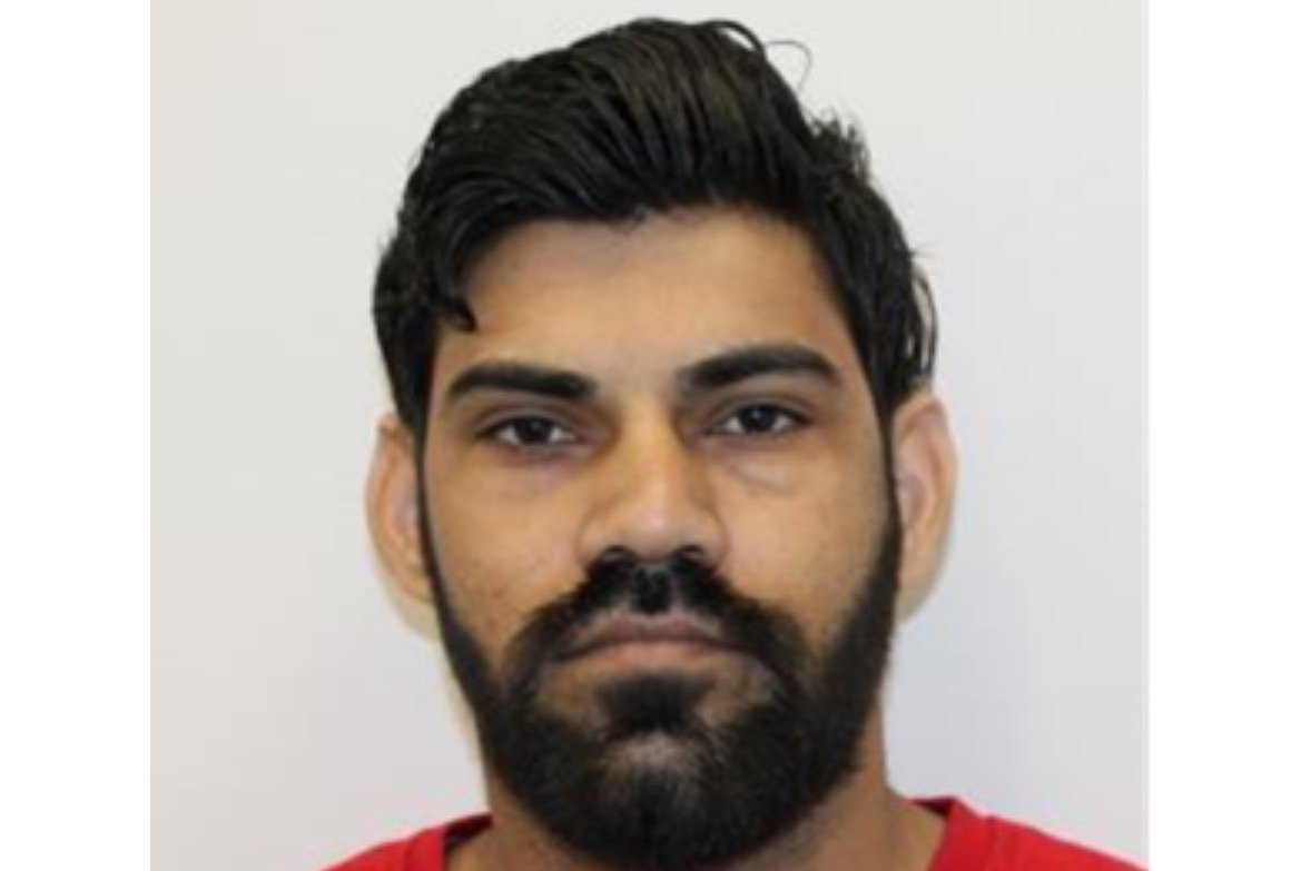 Portrait of a man with a beard and short dark hair, wearing a red shirt, against a plain white background.