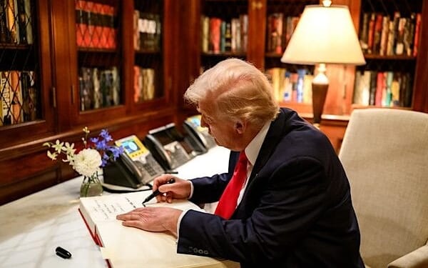 President Donald Trump signs the guest book at the ambassador's residence in Tokyo, Japan on Tuesday, Oct. 28, 2025, as Secretary of Commerce Howard Lutnick, Ambassador George Glass, and his wife, Mary Glass, look on. (Official White House photo by Molly Riley)