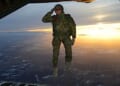 A U.S. soldier assigned to 1st Battalion, 10th Special Forces Group (Airborne) salutes his fellow soldiers while jumping out of a C-130 Hercules aircraft over a drop zone in Germany, Feb. 24, 2015. (U.S. Army photo by Visual Information Specialist Jason Johnston)