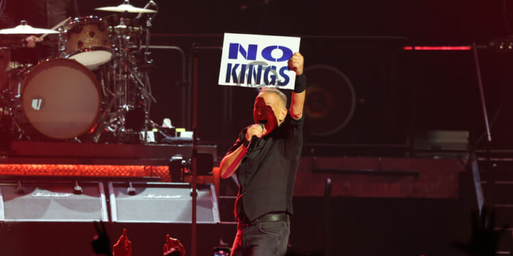 Bruce Springsteen, in concert, holding up a "No Kings" sign.