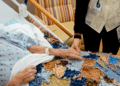 A hospice patient is in bed with her hand being held by a hospice caregiver.