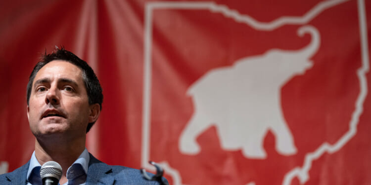 Ohio Secretary of State Frank LaRose speaks in front of a red banner with an elephant inside a map of Ohio.