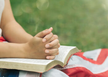 Close-up of young person with flag and Bible on their lap in outdoor setting.