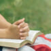 Close-up of young person with flag and Bible on their lap in outdoor setting.