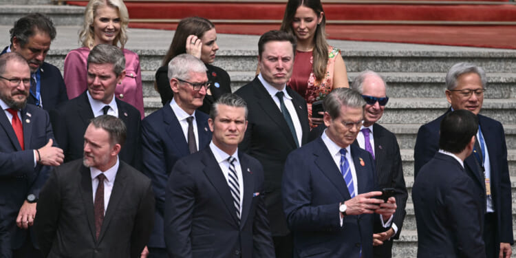 Pete Hegseth and Scott Bessent surrounded by business leaders including Elon Musk and Tim Cook stand on steps.