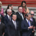 Pete Hegseth and Scott Bessent surrounded by business leaders including Elon Musk and Tim Cook stand on steps.