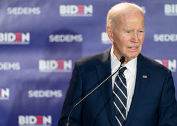 Former President Joe Biden stands at a microphone, with a banner featuring his name and that of "SCDEMS."