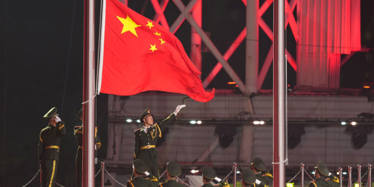 Chinese soldier points to large Chinese flag as row of Chinese soldiers salute.