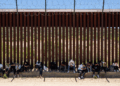 Migrants sit by the iron fence waiting to be processed by the U.S. Border Patrol near the Jacumba Hot Springs after crossing the border.
