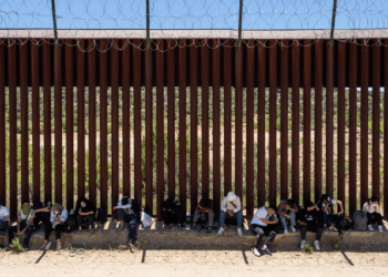 Migrants sit by the iron fence waiting to be processed by the U.S. Border Patrol near the Jacumba Hot Springs after crossing the border.