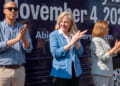 Abigail Spanberger, flanked by Jay Jones and Ghazala Hashmi clap in front of bus during campaign rally.