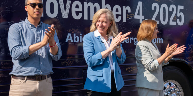 Abigail Spanberger, flanked by Jay Jones and Ghazala Hashmi clap in front of bus during campaign rally.