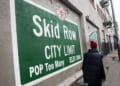 Green sign with white lettering reading "Skid Row City Limit. Pop Too Many."
