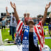 A Black woman draped in American flag and Israeli scarf lifts hands to heaven, with US Capitol in distant background.