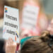 A person holds a sign reading, "Protect trans and nonbinary students!"