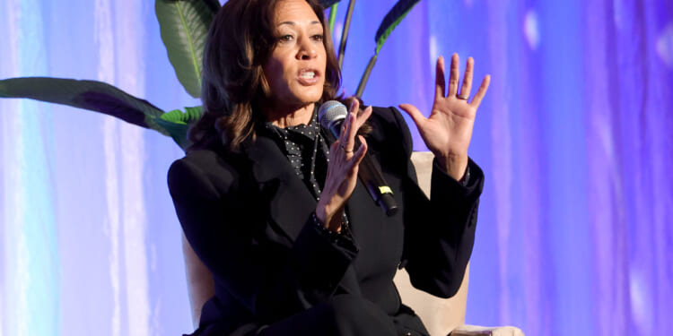 A seated Kamala Harris raises her hands as she makes a point during a talk.