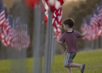 A boy runs among U.S. flags in a field
