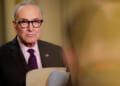 A dour-looking Chuck Schumer holding a file.