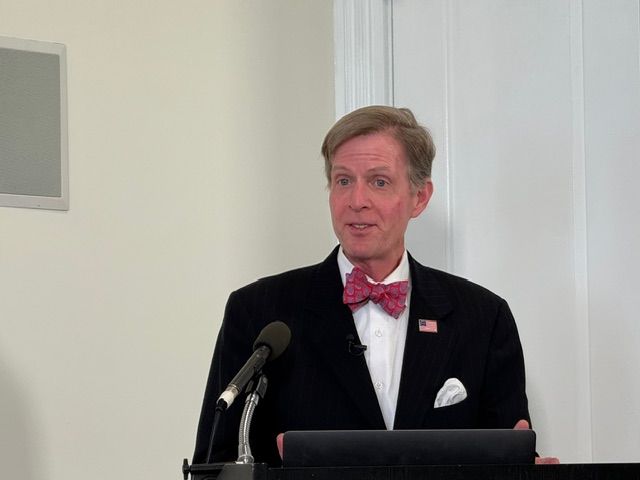 Focus on the Family's Tim Goeglein in black jacket and red bow-tie addresses a room against a white backdrop.