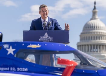 Transportation Secretary Sean Duffy speaking at a podium in front of a car