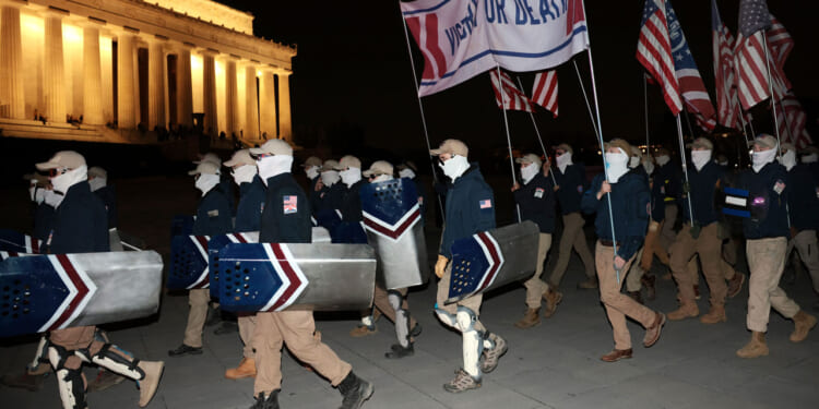 Members of the white nationalist group Patriot Front, wearing masks and carrying shields, gather at the Lincoln Memorial at night.