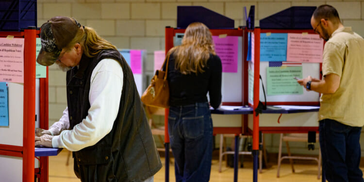 Three people stand at separate voting booths in a room, filling out ballots.