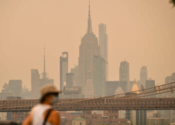 A person wearing a facemark walks near the Brooklyn Bridge as wildfire smoke from Canada causes hazy conditions on July 16, 2026 in New York. Out-of-control wildfires were raging Thursday in the Canadian province of Ontario, prompting evacuations and sending dangerous smoke billowing into the United States where millions of people were exposed to the unhealthy air.