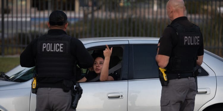 A woman in a car raises her middle finger at two police officers standing outside the vehicle.