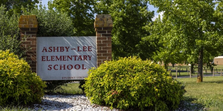 A brick sign reading Ashby-Lee Elementary School stands among green bushes and trees on a sunny day.