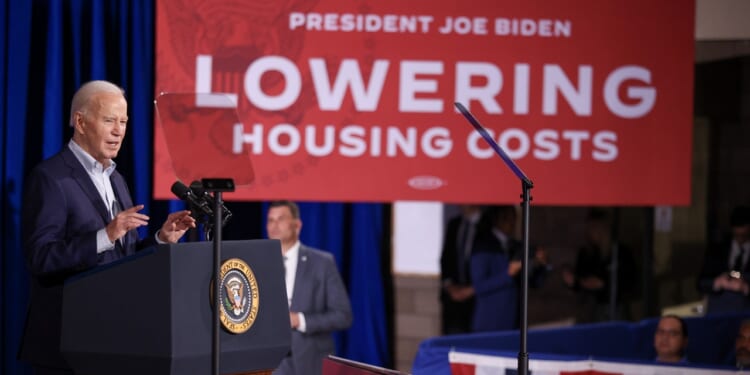 President Joe Biden speaks at a podium with a red sign behind him that reads Lowering Housing Costs during an event.