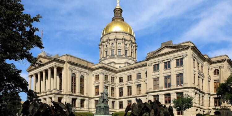 The Georgia State Capitol building with a prominent gold dome under a blue sky, surrounded by greenery and a statue in front.