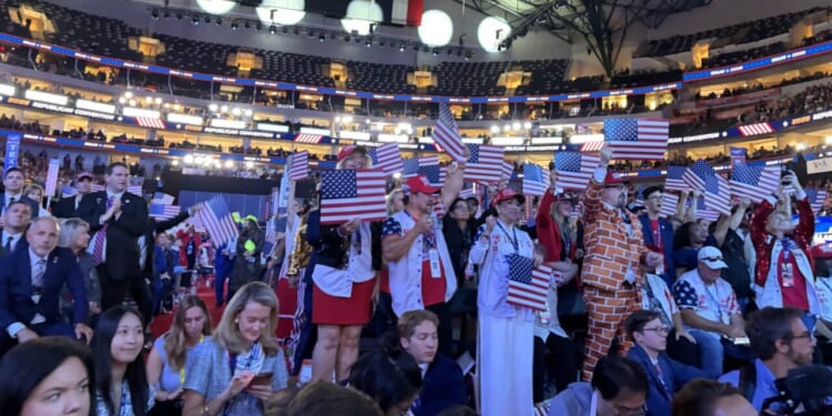 A crowded indoor arena at the Republican National Midterm Convention with people dressed in patriotic outfits, many holding small American flags.