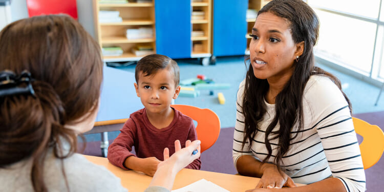 Parental rights concept. Mother speaking with teacher in school. A woman and a young boy sit across from another woman at a table, engaged in conversation in a classroom setting. The boy looks curious while the women appear to be discussing something important.
