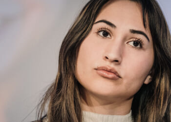 Detransitioner Chloe Cole reveals the dangers of "gender-affirming care" and pediatric gender interventions. Pictured: Cole, a young woman with long brown hair and a neutral expression looks slightly upward. She is wearing a light-colored top and is photographed against a blurred background.