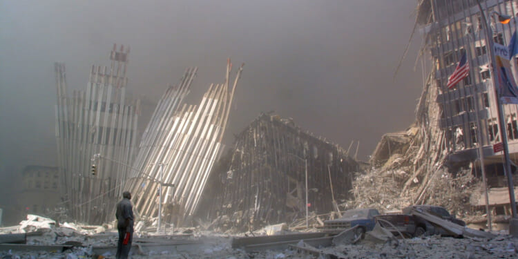 A person stands amid debris and dust clouds, surrounded by partially collapsed skyscrapers and twisted metal in a devastated urban landscape in the aftermath of 9/11.