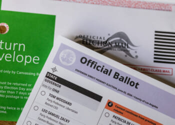 Close-up of a green return envelope, an official election mail envelope, and a partially visible official ballot for a primary election.