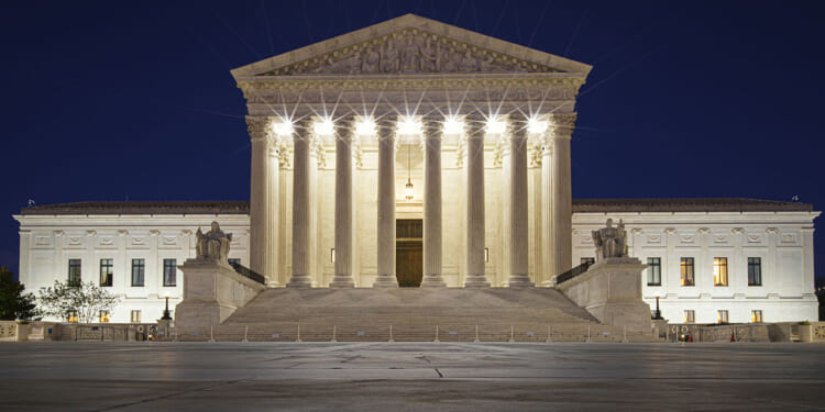 The Trump administration asked the Supreme Court to allow the Bureau of Prisons to cease providing sex-rejecting procedures, citing a memo about the unreliability of the World Professional Association for Transgender Health or WPATH. Pictured: The U.S. Supreme Court building at night, its columns and steps illuminated by bright lights, with statues on either side of the entrance and a dark blue sky in the background.